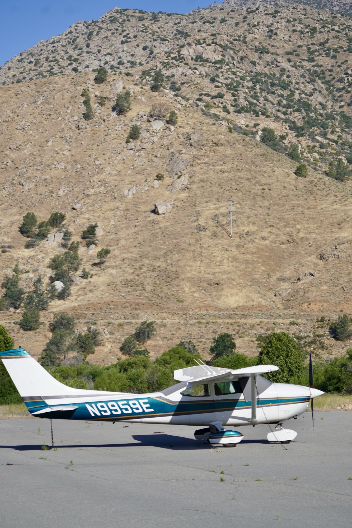 Kern Valley Flyout Cessna 182 N9959E tied down on the ramp at L05, mountains rising behind it.
